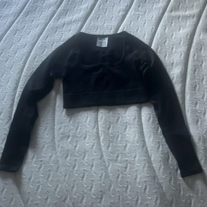 Svart topp från Aimn - Svart topp från Aimn i ett stretchigt och ribbat material. Toppen har lång ärm och en snygg fyrkantig halsringning. Perfekt att slänga över sport-bh eller linne för en cool look. Materialet är 92% polyamid och 8% elastan. Endast tvättad en gång ej använd. 