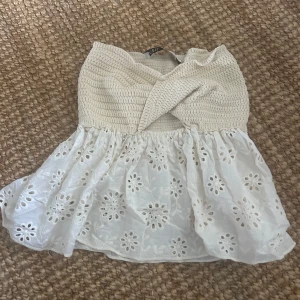 Vit broderad bandeau tubtopp - Supersöt vit bandeau tubtopp med broderade blommor och hålmönster Överdelen är ribbad och smockad med omlott-detalj framtill. Använd fåtal gånger
