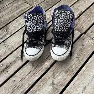 Converse All Star leopardmönstrade sneakers - Säljer ett par Converse All Star high-top sneakers i storlek 37 med svart och vit leopardmönster. Skorna har lila textilfoder, svarta snören och klassisk rund tå. Yttermaterialet är bomullstextil och sulan är vit med svart rand. Perfekt för dig som vill sticka ut med coola detaljer.