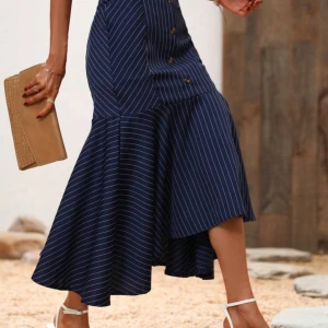 Marinblå randig långkjol med knappar - Snygg marinblå långkjol med vita ränder och asymmetrisk volangkant. Kjolen har dekorativa knappar framtill och en figurnära passform upptill som övergår i ett flödande, voluminöst fall. Perfekt för dig som gillar en trendig och elegant look.