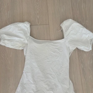 Vit puffärm topp från H&M - Säljer en vit topp från H&M i storlek S med puffiga korta ärmar och fyrkantig halsringning. Toppens material är mjukt och stretchigt, perfekt för dig som gillar en clean och trendig look. Passar dig som vill ha något enkelt men ändå med coola detaljer.