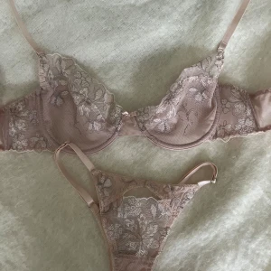 Blommig spetsbyxor och trosor från Before The Dawn - Superfin bh och trosor från Before The Dawn i ljusrosa med blommig spets och tunna axelband. Både överdel och underdel har transparenta partier med broderade blommor och en liten rosett framtill. Perfekt för dig som gillar romantisk och feminin stil. Bh-n i storlek m och trosorna i s