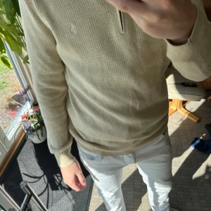 Beige half zip tröja från Ralph Lauren - Säljer en beige långärmad tröja från Ralph Lauren med half zip och diskret broderad logga på bröstet. Tröjan har en stickad struktur och ribbade muddar vid ärmslut och nederkant. Perfekt för dig som gillar klassisk och clean stil.
