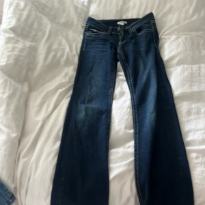 Mörkblå bootcut jeans från Gina Tricot - Säljer ett par mörkblå jeans från Gina Tricot med bootcut passform. Jeansen har vita kontrastsömmar, klassiska fickor fram och bak samt knapp- och dragkedjestängning. Perfekta för dig som gillar en lite vidare modell nertill.