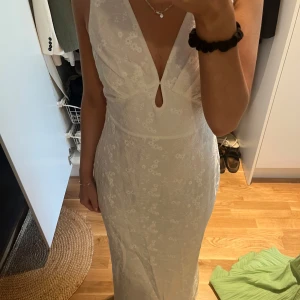 Vit långklänning med blommigt mönster från Adoore - Superfin vit långklänning från Adoore med  blommigt mönster och djup v-ringning. Klänningen har ärmlös design och liten öppning framtill. Aldrig använd. 