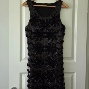 Paljettklänning - Svart klänning med paljettdetaljer framtill. Klänningen har rund halsringning och är figurnära