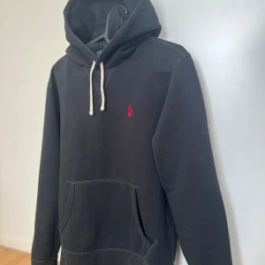 Ralph Lauren Hoodie - Svart hoodie från Polo Ralph Lauren. Klassisk känguruficka framtill och mjukt material som känns skönt mot huden. Perfekt för en avslappnad stil. Storleken är XS och passar bra till folk som är runt 170-175cm