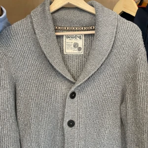 Grå stickad kofta / cardigan - Säljer en grå stickad kofta med bred krage och två knappar framtill. Koftan har lång ärm och är ribbstickad för en klassisk look. Perfekt att slänga på sig när det är kyligt ute.