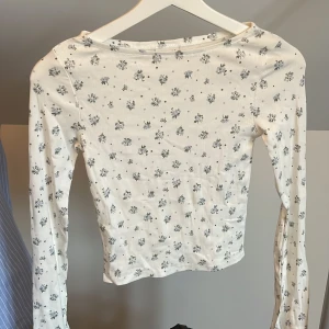 Vit blommig långärmad topp från Kappahl - Säljer en söt vit långärmad topp från Kappahl med små blå blommor och ribbad struktur. Perfekt för dig som gillar en feminin och enkel stil. Toppen har en tight passform och är superfin till jeans eller kjol. Utvängda armar med en slit i ärmen💞endast testad