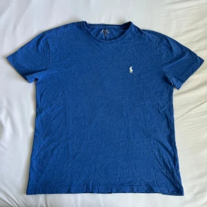 Blå t-shirt från Polo Ralph Lauren - Säljer en klassisk blå t-shirt från Polo Ralph Lauren med broderad vit logga på bröstet. T-shirten har rund halsringning och korta ärmar. Perfekt för en stilren och avslappnad look.