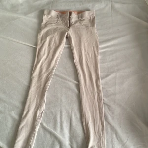 Beige tighta byxor från Freddy WR.UP - Säljer ett par beige tighta byxor från Freddy WR.UP med låg midja. Byxorna har dragkedja och två knappar framtill samt dekorativ detalj vid fickan. Perfekta för dig som gillar en slim och figurnära passform. Nypris är runt 700kr