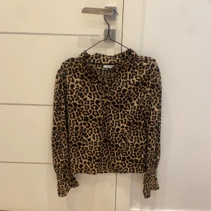 Leopardmönstrad blus med volangkrage - Säljer en snygg leopardmönstrad blus med volangdetalj och knytning vid kragen. Blusen har långa ärmar och är i ett mjukt, lätt material. Perfekt för dig som vill sticka ut lite extra!