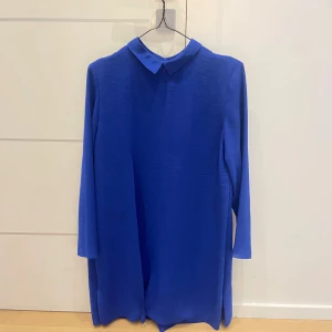 Kornblå klänning med krage - Säljer en kornblå klänning med klassisk krage och långa ärmar. Klänningen har en rak passform och stängs med dragkedja i ryggen. Perfekt för dig som gillar stilrena och enkla plagg med en poppig färg.