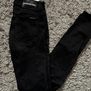 Calvin Klein Jeans - Säljer ett par svarta jeans från Calvin Klein Jeans med klassisk femficksdesign och tydlig logotyp på bakfickan. Jeansen är en skinnymodell med lite slintningar som detalj vid bensluten! Använd antal gånger!💕