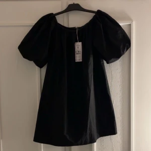 Svart klänning med puffärmar  - Svart off-shoulder klänning med puffiga ärmar och en löss passform. Slutsåld på Ginas hemsida, helt oanvänd med prislappen kvar 