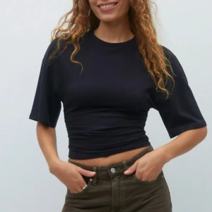 Svart t-shirt går in i midjan - Säljer en svart croppad t-shirt med halvlånga ärmar och rund halsringning. Toppen har en tight passform och är enkel att matcha till olika outfits. Perfekt för dig som gillar en stilren och basic look.