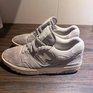 Grå Suede New Balance 550 sneakers *LIMITED EDITION* - Säljer ett par grå New Balance 550 sneakers i grå suede med klassisk N-logga på sidan. Skorna har snörning och en platt sula, perfekt för en stilren vardagslook. Tidlös design med diskreta detaljer och bekväm passfo