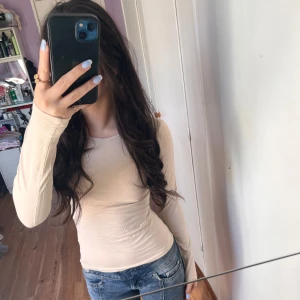 Beige långärmad topp från H&M - Säljer en enkel och stilren beige långärmad topp från H&M. Toppen har tight passform och är tillverkad i ett mjukt bomullsmaterial. Perfekt att matcha med jeans eller kjol för en clean look.