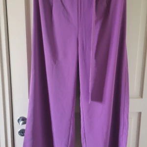 Lila vida byxor från SHEIN - Säljer ett par lila vida byxor från SHEIN i storlek XL. Byxorna har en lös passform och är tillverkade i ett mjukt syntetmaterial. Perfekta för dig som gillar färg och vill ha något bekvämt och trendigt.