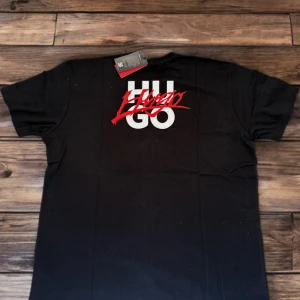 🔥💙Helt Ny-Fynda en snygg HUGO T-shirt - Säljer en helt ny och oanvänd HUGO T-shirt med snyggt tryck på både fram- och baksidan. Perfekt för dig som vill ha en modern och stilren look! Produktinformation: 	•	Material: 100% härlig bomull som känns mjuk mot huden. 	•	UV-skydd: Tyget ger ett skydd mot solens UV-strålar, vilket är extra bra under soliga dagar.