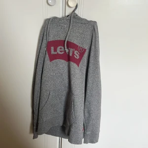 Grå hoodie från Levi's - Säljer en klassisk grå hoodie från Levi's med röd logga framtill. Tröjan har huva med dragsko och en stor magficka. Perfekt för en avslappnad stil.