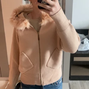 Beige stickad jacka med päls - Mysig beige stickad jacka med huva och fuskpälsdetalj. Jackan har dragkedja framtill och fickor. Perfekt vår och höst jacka. Den är köpt i Thailand så har inget vanligt märke. Jag har ALDRIG andvöndt den, lappen är kvar💕