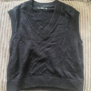 Svart stickad väst med v-ringning - Svart stickad väst från Bik Bok med bred ribbad v-ringning och ribbade kanter. Perfekt att styla över en skjorta eller t-shirt för en trendig lager-på-lager-look.