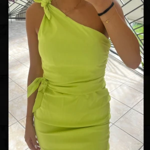 Limegrön oneshoulder-klänning från Zara - Säljer en limegrön, figurnära klänning från Zara med oneshoulder och knytband vid axeln och midjan. Klänningen har en snygg, slät yta och är perfekt för dig som vill sticka ut med färg. Pris går att diskutera. 