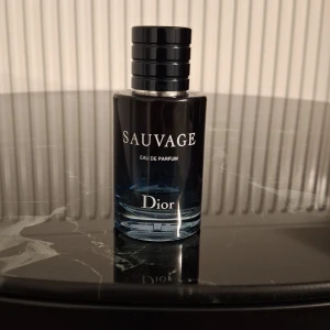 Sauvage Eau de Parfum från Dior - Säljer en lyxig herrparfym, Sauvage Eau de Parfum från Dior. Flaskan är mörkblå med svart lock och har tydlig Dior-logga på toppen. Parfymen har en elegant och modern design, perfekt för dig som gillar exklusiva dofter.