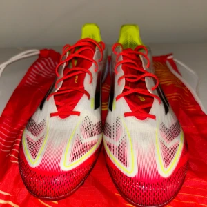 Adidas F50 Elite fotbollsskor i rött och vitt - Säljer ett par Adidas F50 fotbollsskor i vitt, rött och gult med svarta detaljer. Skorna har snörning och en platt sula med dobbar för bra grepp på planen. Perfekta för dig som vill sticka ut på fotbollsplanen! Använda 1 gång och jag pustar även till de innan jag skickar iväg de 😁