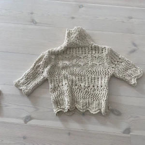 Beige stickad polotröja - Säljer en beige stickad polotröja med vackert hålmönster och trekvartsärm. Tröjan har en hög krage och är perfekt för lager-på-lager-stil. Mjuk och mysig känsla, passar till många outfits.