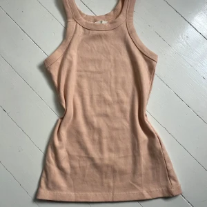 Aprikosfärgat ribbad linnetopp - Säljer en aprikosfärgad ribbad linnetopp med rund halsringning och ärmlös design. Toppen har en tight passform och är perfekt för varma dagar eller som lager under en skjorta. Aldrig använd. Skriv för fler bilder💞