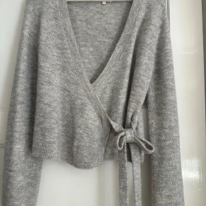 Grå omlottkofta från Gina Tricot - Populär tröja från gina i stl M, sitter jätte fint, använd två gånger. Skriv om du har fler frågor 💗