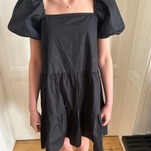 Svart puffärm klänning - Säljer en svart klänning med puffärmar och fyrkantig ringning. Är från HM och är i storlek XS! Lös passform och 3 volanglager