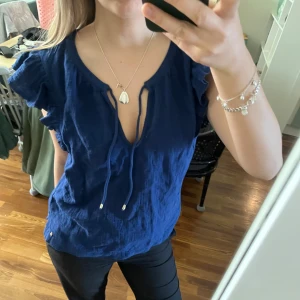 Mörkblå top - Säljer en mörkblå linnetopp från Loveit med volangärmar och knytning fram. Toppen har en luftig passform och är perfekt för varma dagar. Snygg och enkel att matcha till olika outfits.