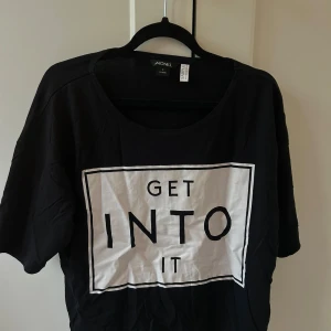 Svart t-shirt med tryck från Monki - En cool croppad t-shirt från Monki i storlek S med stort vitt tryck på framsidan där det står 'GET INTO IT' i svart text. 😍💕