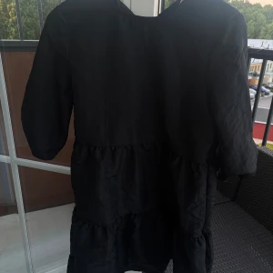 Svart volangklänning med trekvartsärm - En svart klänning med volangdetaljer och trekvartsärmar. Klänningen har en lös passform.