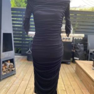 Svart mesh långklänning med rynk S - Svart, figurnära klänning med rynkade detaljer och trekvartsärmar. Klänningen har en elegant, off-shoulder design som framhäver axlarna. Perfekt för festliga tillfällen. Längd: 105 cm ﻿Bystvidd: 40 cm ﻿Nylon/viskos.  Inga bilder när den sitter på mig! Katter finns i hemmet!