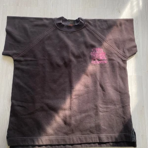 Svart t-shirt Converse L - Cool svart t-shirt från Converse i lila framtill och grönt baktill. Oversized fit med korta ärmar och rund hals. Perfekt för dig som gillar streetwear.