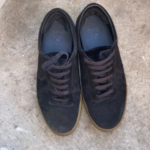 Svarta sneakers från Axel Arigato - Snygga svarta sneakers från Axel Arigato i mocka med bruna gummisulor. Klassisk låg modell med rund tå och svarta snören. Perfekta för dig som gillar stilrena och tidlösa skor med en modern touch. De är sparsamt använda och köptes ca 2 månader sedan!! 