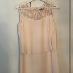 Ljus ärmlös klänning med spetsdetalj - Superfin baby rosa/persika aktig färg klänning med en transparent spets upptill och snygg layering-effekt. Rund halsringning och knapp i nacken. Perfekt för sommarens alla tillfällen när du vill känna dig extra söt och stilren. Helt oanvänd, väldigt synd att en söt klänning bara ska stå i garderoben så hoppas den kommer till användning i någon annans ägo☺️ storlek 34-36. Skriv vid frågor! 