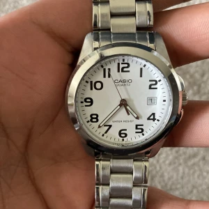 Casio silverfärgad armbandsklocka - Klassisk Casio armbandsklocka med rund vit urtavla, tydliga svarta siffror och datumvisning. Klockan har ett stilrent armband i silverfärgat rostfritt stål och quartz-urverk. Perfekt för dig som gillar enkel och tidlös design. Säljer en äkta casio klocka har avänt den bara några få gånger utan prislappen ( kan gå ner i priset )