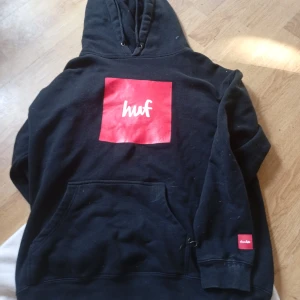 Svart HUF & Chocolate skateboards. hoodie med röd logga - Svart hoodie från HUF med stor röd fyrkantig logga på ryggen och mindre röd detalj med 'chocolate' på ärmen. Klassisk huva med snörning och stor magficka. Perfekt streetwear-vibe och riktigt skön passform.