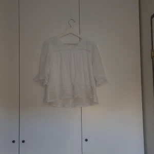 Vit blus från Gina Tricot - Söt vit blus från Gina Tricot i luftig bomull. Blusen har trekvartsärmar med lätt volang och v-ringning framtill. Fina spetsdetaljer och avslappnad passform gör den perfekt till jeans eller kjol.