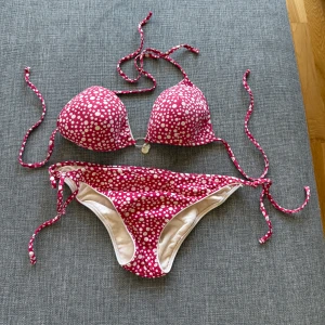 Rosa prickig bikini med knyt - •Snygg bikini i rosa med vita prickar.  •Överdelen är en klassisk trekantsmodell med knyt i nacke och rygg samt en liten silverfärgad ringdetalj framtill.  •Underdelen har knyt i sidorna för perfekt passform. •Perfekt för strandhäng och poolparty! •Storlek S. Mycket bra skick. Tvättad. •Djurfritt och rökfritt hem.
