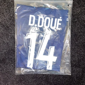 PSG D. Doué matchtröja Jordan S - Paris Saint-Germain fotbollströja med D. Doué och nummer 14 på ryggen. Tröjan är blå med vita detaljer, har korta ärmar och är tillverkad i ett lätt och ventilerande material. Framsidan har Qatar Airways-logga och PSG-emblem. Snygg design med Jordan-logga på bröstet.