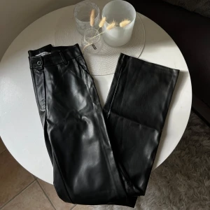 Svarta skinnbyxor från Madlady - Snygga svarta byxor i skinnimitation från Madlady. De har hög midja och bootcut. Byxorna stängs med knapp och dragkedja och har en clean look som passar till allt. Endast använd en gång.