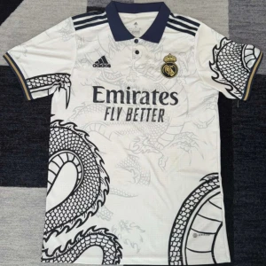 Real Madrid x Adidas drakmönstrad tröja  - Snygg Real Madrid fotbollströja från Adidas i vitt med mörkblå detaljer och coolt drakmönster. Tröjan har korta ärmar, pikékrage och broderade klubb- och Adidasloggor. Materialet är lätt och andas, perfekt för match eller träning.