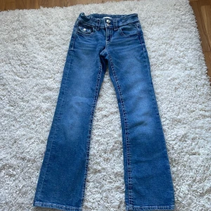 Blå jeans från Gina Tricot, stl 152 - Snygga blå jeans från Gina Tricot i klassisk modell med raka ben och normal passform. Jeansen har dubbla knappar i midjan, fem fickor och tydliga kontrastsömmar. Perfekta för dig som gillar en enkel och tidlös stil.
