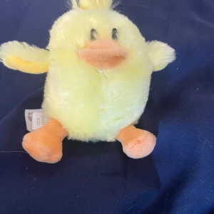 Gullig liten bebis kyckling - Bilderna visar en söt, gul plyschkyckling från Teddykompaniet. Den är liten nog att rymmas i handen och har mjuk päls, orange näbb och fötter. Perfekt som present eller dekoration. 